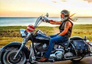 A photo of an old bearded guy with long white hair riding his cruiser motorcycle with a helmet and a leather vest